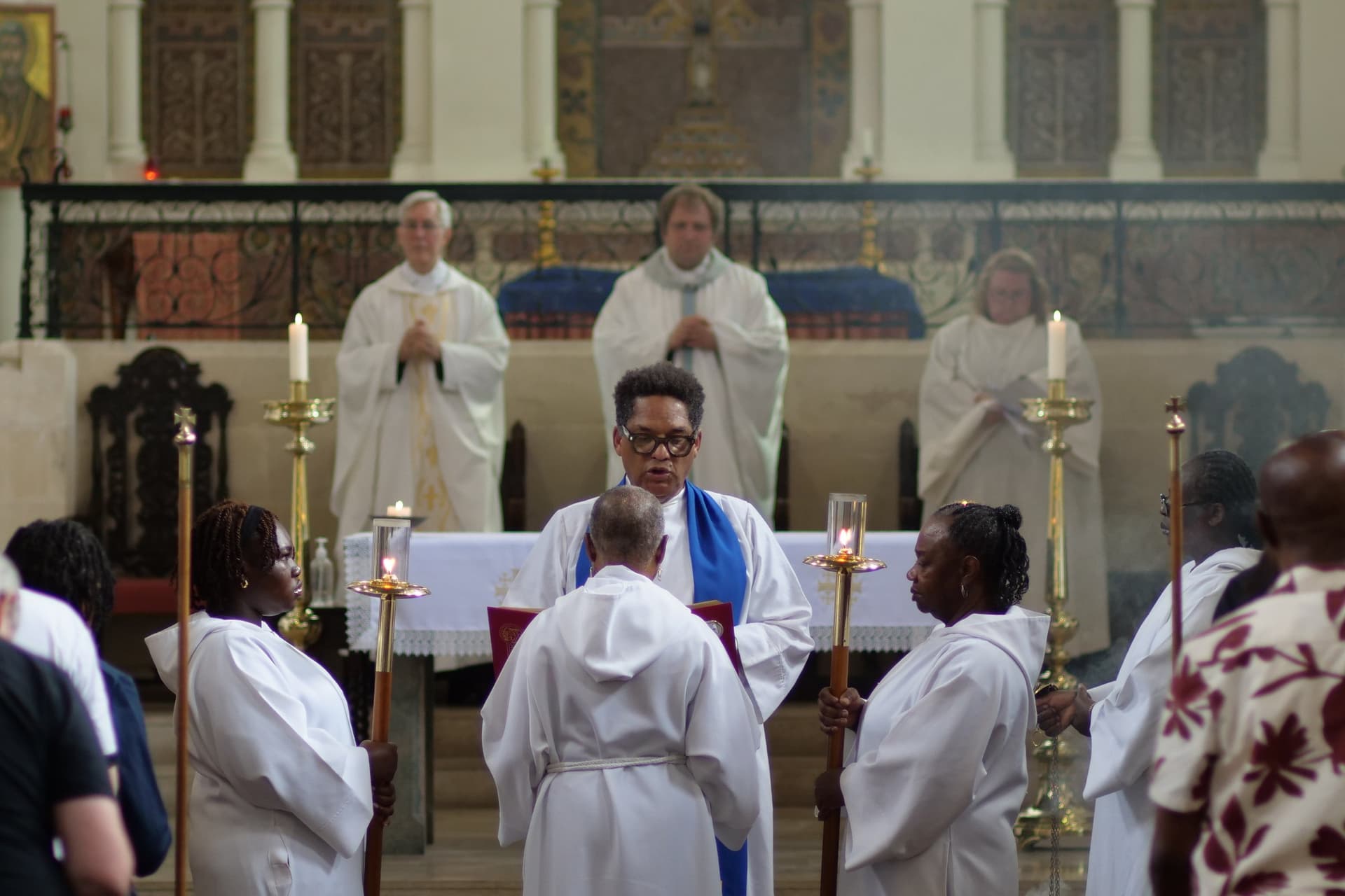 The gospel being read in the middle of the congregation at the Sunday Sung Family Mass, with servers holding candles on either side.